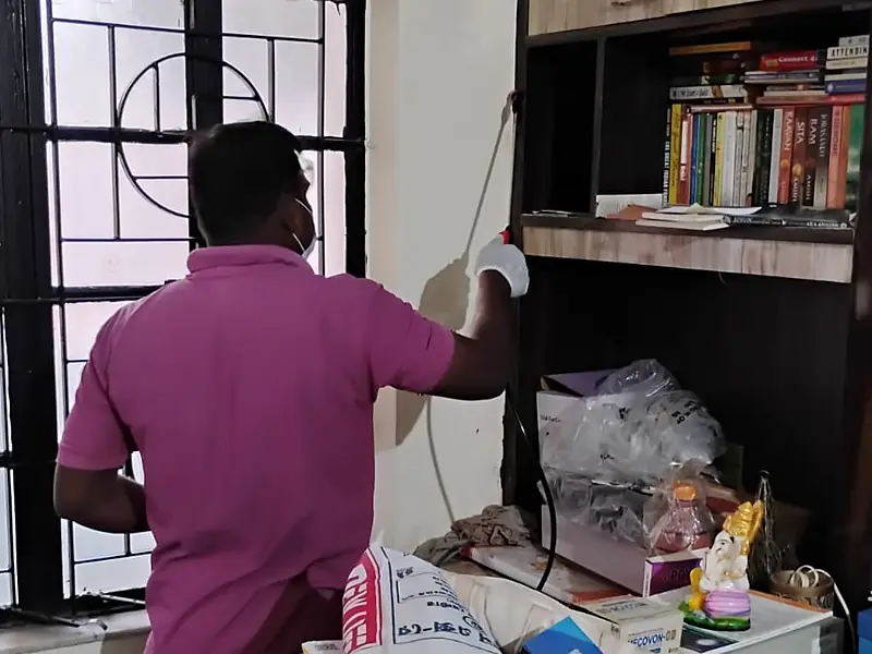 Technician applying herbal cockroach and ant treatment beside a window and bookshelf