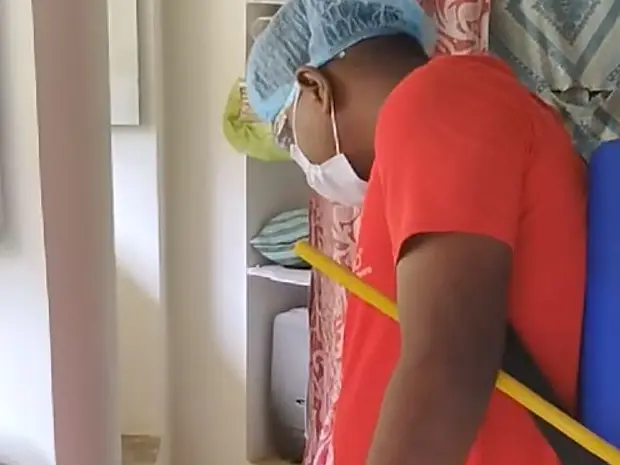 Pest control technician in a cap and mask carrying a backpack sprayer