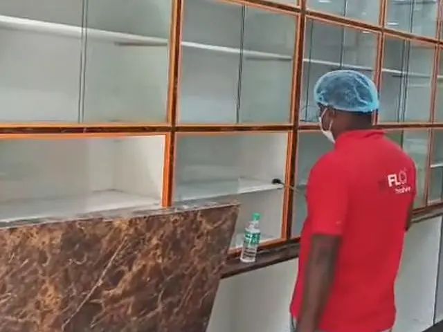 Technician in cap and mask spraying inside a commercial space with glass cabinets